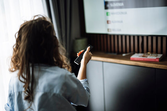 A person watching television at home while holding a remote control