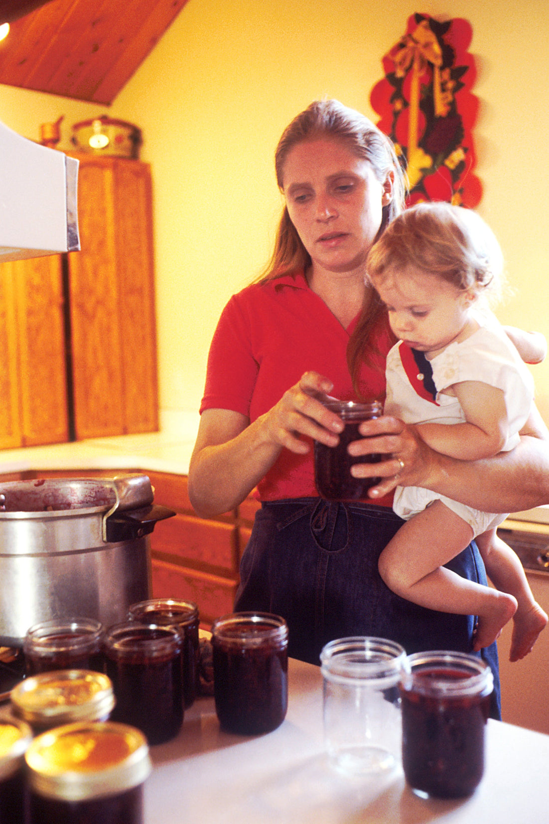 A mother holding her young child in a home kitchen, used as an editorial image for sober motherhood and recovery.